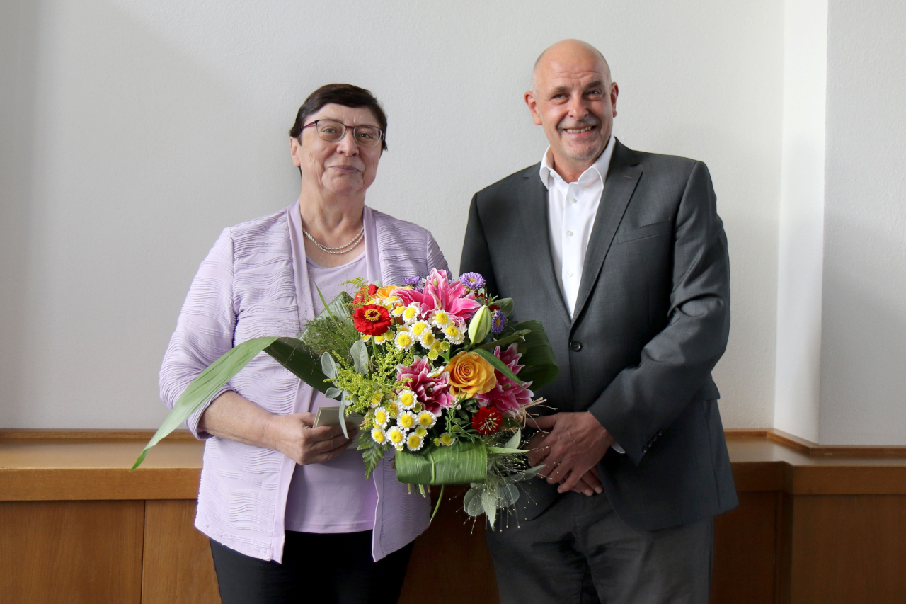 Zu sehen ist ein Bild von Prof. Orthun Riha mit einem Blumenstrauß. Neben ihr steht Prof. Ingo Bechmann als Vertreter des UKLs.